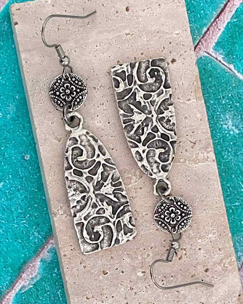 Silver textured Earrings displayed on stone slab.